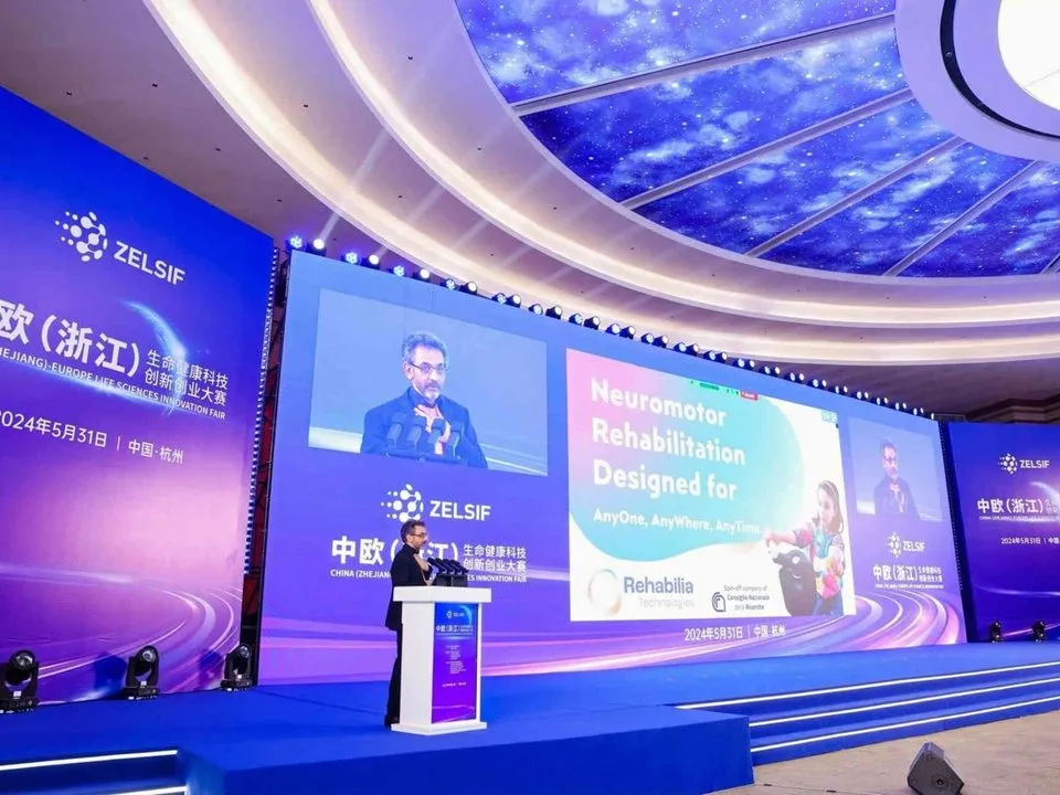 Matteo Malosio presents PhiCube on stage at ZELSIF in Hangzhou, China, in front of a slide on neuromotor rehabilitation.