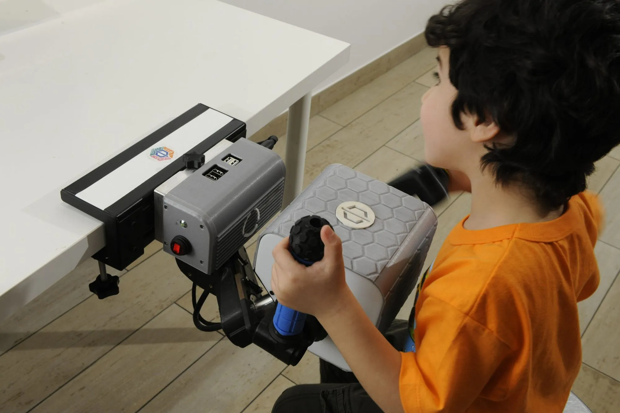 Un niño sujeta una empuñadura montada en la unidad robótica PhiCube, fijada al borde de una mesa.