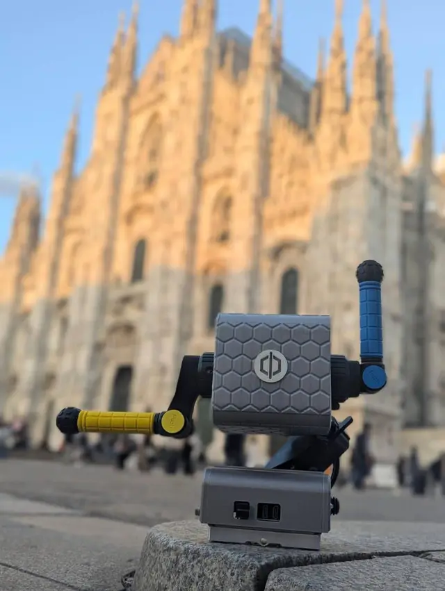 The PhiCube device rests on a stone ledge in Piazza Duomo, Milan, with the cathedral façade lit at sunset behind it.