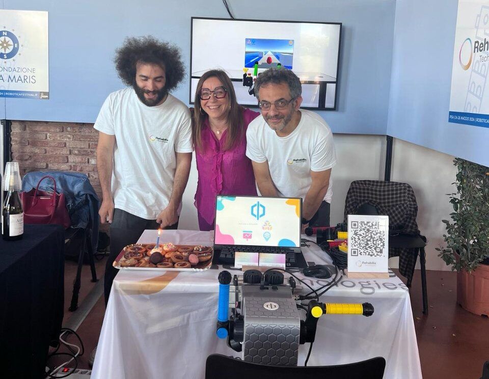 Trois membres de l’équipe derrière une table où trône un gâteau aux bougies allumées, pour le premier anniversaire de Rehabilia sur le stand du festival.