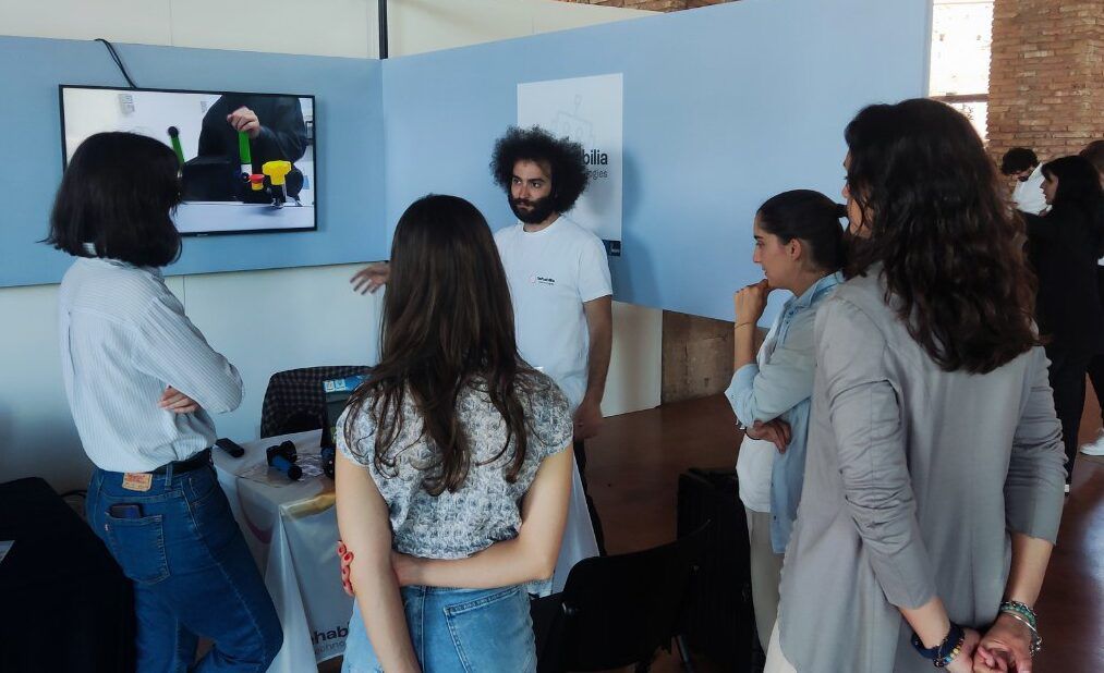Un membre de l’équipe présente PhiCube à des visiteurs, devant un écran qui diffuse une vidéo de démonstration.