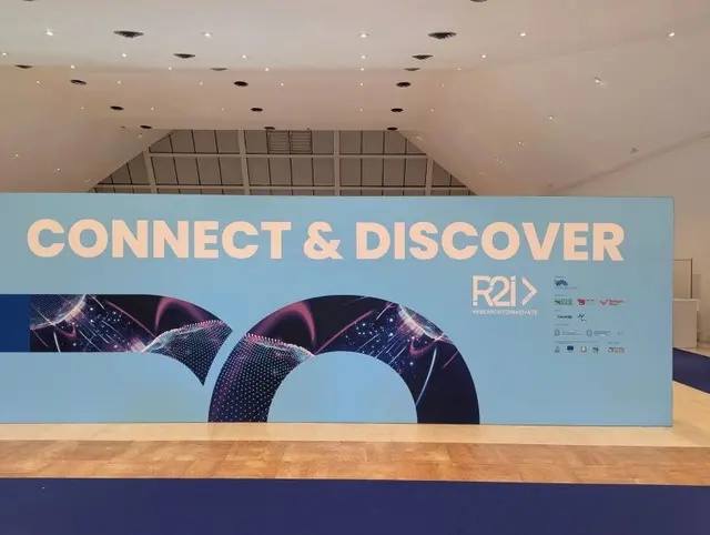 A wall reading "Connect & Discover" with the R2I – Research to Innovate logo, at the Ex GAM in Bologna.