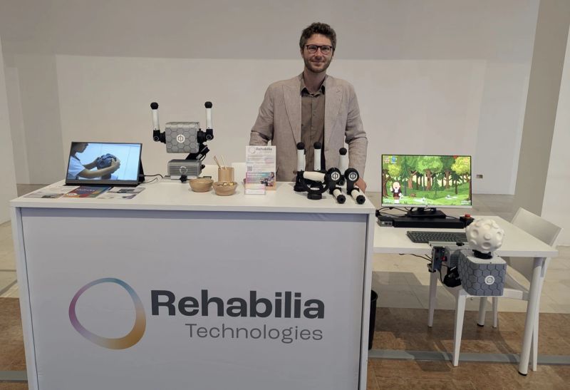 Der Stand von Rehabilia Technologies auf der R2I 2026: Griffe und Robotereinheit von PhiCube auf dem Tresen, auf einem Bildschirm läuft ein Spiel.