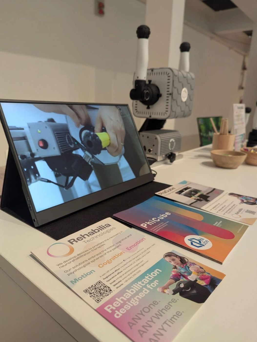 Die Robotereinheit von PhiCube, ein tragbarer Bildschirm und Informationsmaterial am Stand von Rehabilia Technologies auf der R2I 2026.