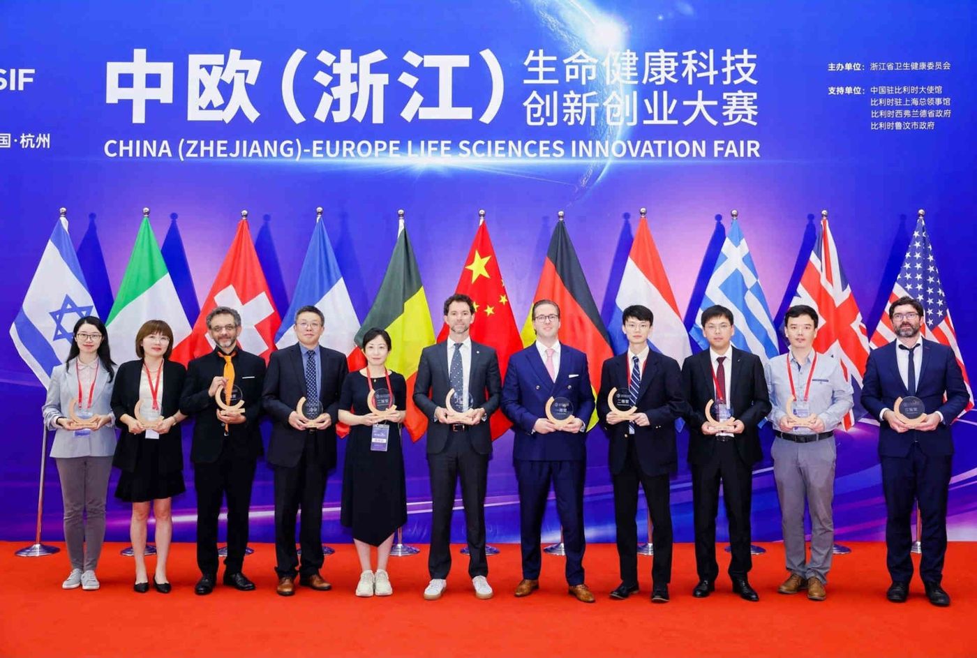 Vertreterinnen und Vertreter der ausgezeichneten Unternehmen posieren bei der Preisverleihung der ZELSIF in Hangzhou mit ihren Trophäen vor Nationalflaggen.