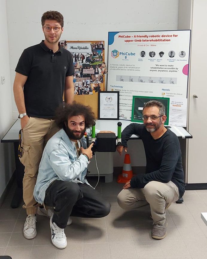 Die drei Mitgründer posieren im Büro neben einem Poster über PhiCube – zur Gründung von Rehabilia Technologies.